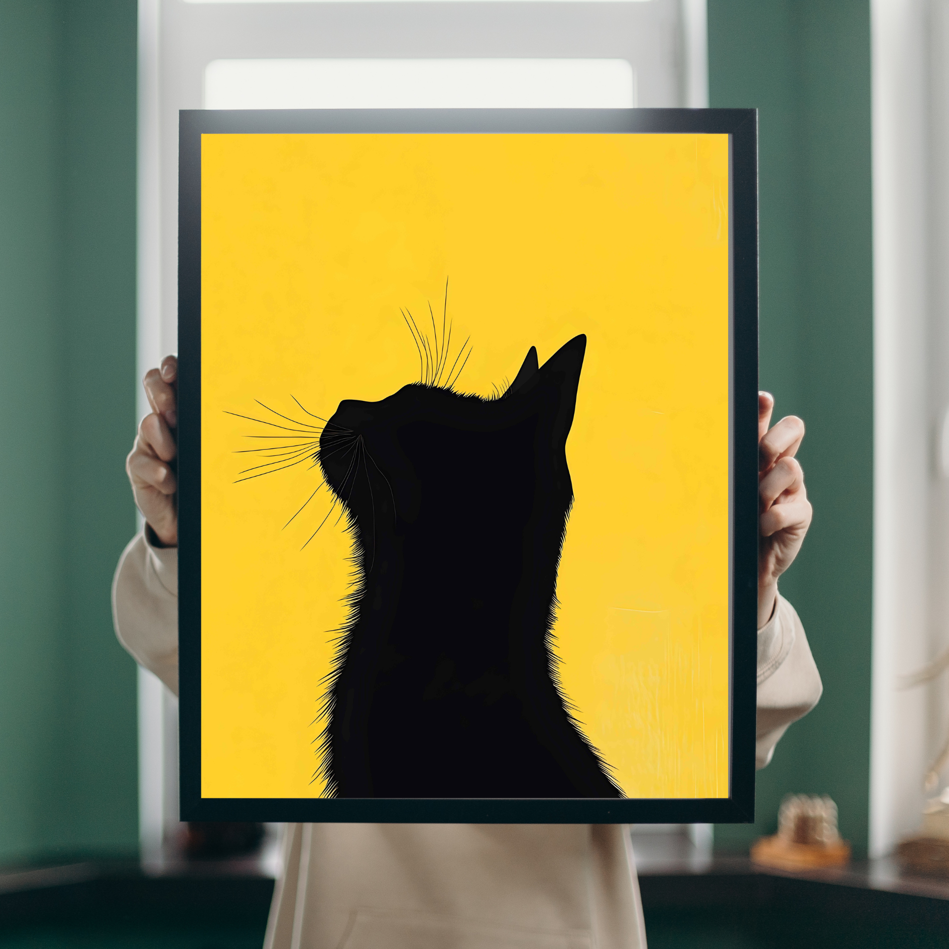 Framed artwork of a black cat silhouette on a yellow background held by a person.